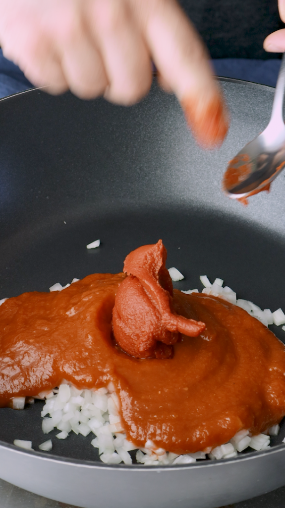 Next add diced onion, tomato sauce, tomato paste, minced garlic, turmeric, and coriander to a large pan. 